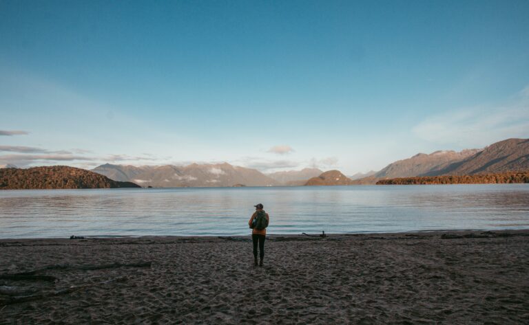 a person standing on a beach with a body of water and mountains in the background